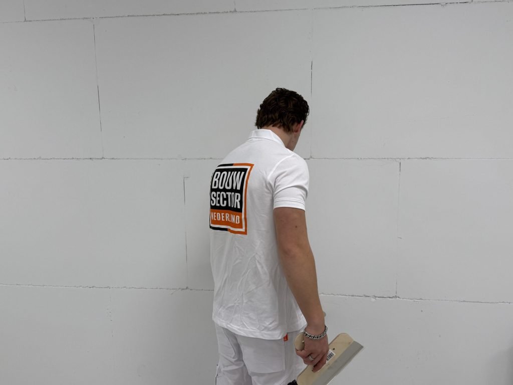 Stukadoor met een spaan in de hand bekijkt de naden van een kale muur voordat hij gaat pleisteren