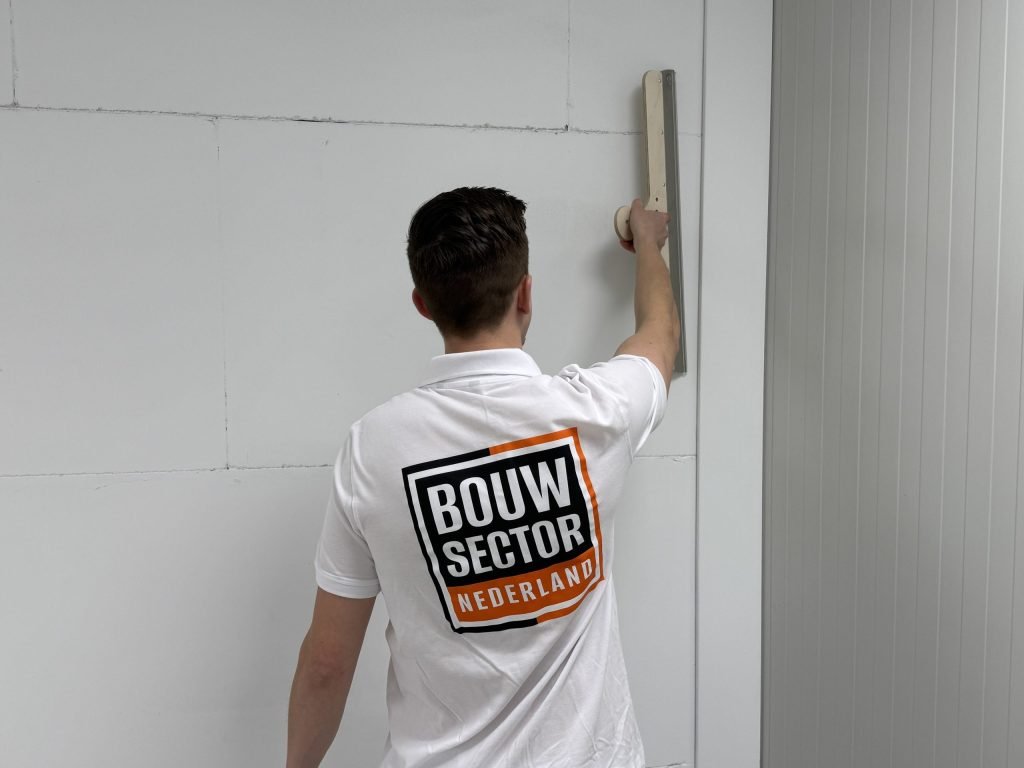 Stukadoor met het logo van Bouwsector Nederland op zijn rug strijkt een wand glad tot vlak onder het plafond