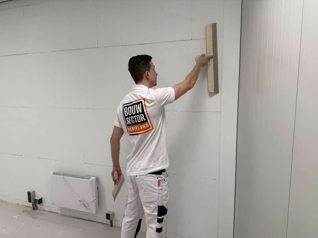 Stukadoor van Bouwsector Nederland trekt met een lange spaan een wand vlak, met de kleine spaan nog in zijn andere hand