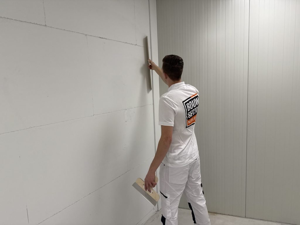 Vakman haalt een rei langs een lange muur van kalkzandsteen om te zien waar de wand nog hol of bol staat