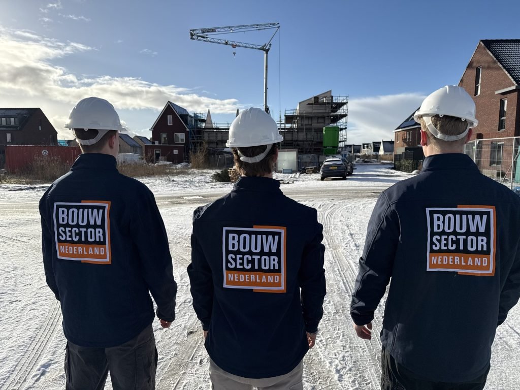 Drie medewerkers van Bouwsector Nederland met bouwhelm kijken naar een straat met huizen in aanbouw