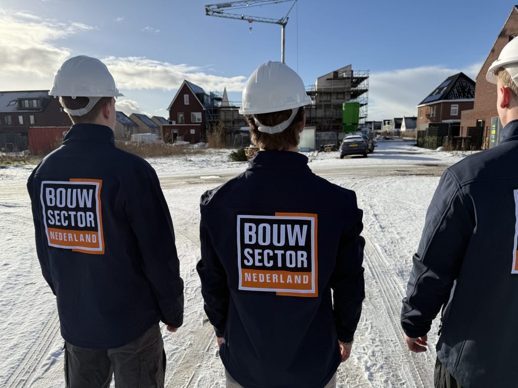 Drie vakmensen van Bouwsector Nederland met witte helm op weg naar een rij nieuwe woningen in de sneeuw